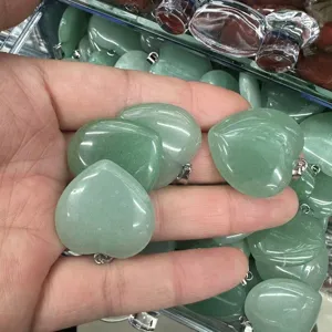 Close-up of green heart-shaped stone pendants with metal bails in hand
