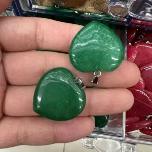 Close-up of two green heart-shaped crystal semi-precious stone pendants held in hand.