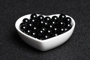 Close-up of polished natural black agate loose beads in a white heart-shaped ceramic dish