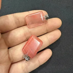 Vista detallada de dos colgantes rectangulares de piedra natural rosa sostenidos en mano