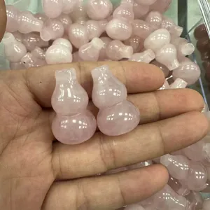 Eine Hand hält zwei natürliche rosa Rosenquarz-Kürbis-Anhänger für DIY-Schmuck