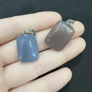 Detalle de dos colgantes rectangulares de ágata natural gris sostenidos en la mano para escala.