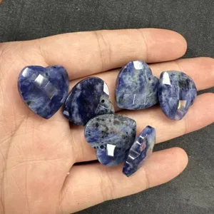Nahaufnahme von facettierten blauen Naturstein-Herzanhängern in der Hand für DIY-Schmuck