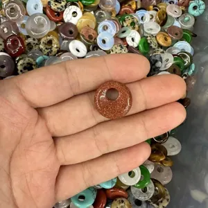 Close-up of a goldstone donut bead held in hand with assorted crystal stones background.