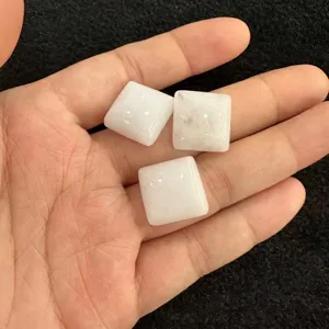 Nahaufnahme von drei quadratischen weißen Quarzstein-Kabochons in der Handfläche