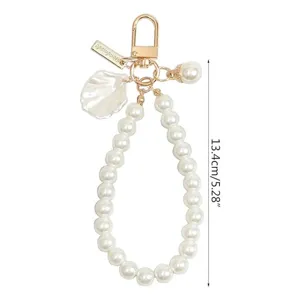 Close-up detail of white pearl keychain with delicate shell pendant and gold clasp.