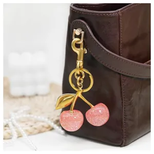 Detailed close-up of a sparkling pink cherry bag charm hanging on a stylish leather bag.