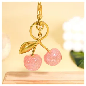 Close-up of a glittering pink cherry keychain with gold hardware, stylish bag charm accessory.