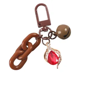 Detalle de llavero de cadena marrón, colgante de cristal rojo en gota y campanita linda.