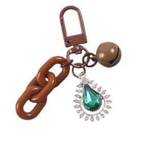 Close-up of DIY keychain accessory with brown chain, bell, and green teardrop crystal pendant.