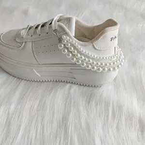 White casual sneaker detail featuring a multi-layer pearl chain accessory and clean leather upper.