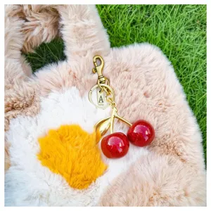 Detailed view of shiny red resin cherry keychain accessory with letter pendant on fuzzy bag.