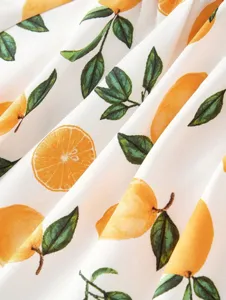 Close-up detail of smooth white fabric featuring vibrant yellow citrus fruit and green leaf print.