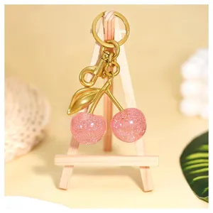 Detailansicht des glitzernden rosa Kirschen-Schlüsselanhängers mit goldenem Metallblatt und Haken.