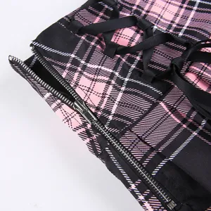 Detailshot van een roze met zwarte geruite plooirok in punkstijl met ritssluiting en vetersluiting.