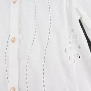 Detailed view of white embroidered blouse, long sleeve floral hollow out shirt trim.