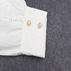 White long sleeve blouse detail showcasing delicate embroidery and elegant pearl button cuffs.