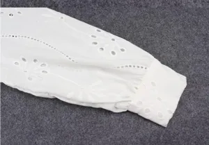 Close-up detail of women white long sleeve top with floral embroidery and elegant puff sleeves.