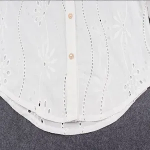 Close-up detail of white eyelet embroidered long sleeve button-up shirt with delicate floral design.