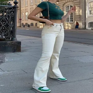 Completo estivo donna con crop top corto e pantaloni a zampa bianchi, stile streetwear casual.