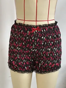 Primo piano di pantaloncini smockati con stampa a ciliegie, pizzo e fiocco rosso.