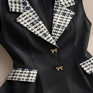 Primo piano di gilet da donna nero con risvolto pied de poule e bottoni con fiocco dorati.