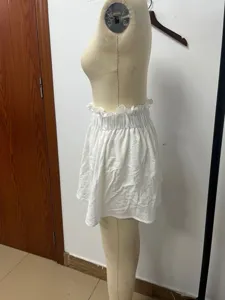 Dettaglio della vista laterale di una gonna corta da donna bianca con volant su manichino.