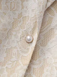 Close-up detail shot of the beige lace vest, highlighting delicate floral lace and pearl button.