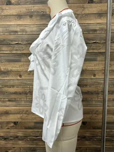 Side view detail of a white long sleeve V-neck blouse with elegant floral pattern and ruffles.
