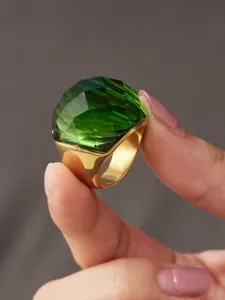 Nahaufnahme des markanten, klobigen grünen Glassteinrings mit poliertem vergoldetem Edelstahlband.