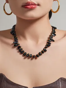 Nahaufnahme der schwarzen Perlenkette mit Goldzwischenteilen und eleganten runden Ohrringen.