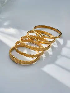 Close-up detail of stacked gold-plated stainless steel bangles featuring floral designs