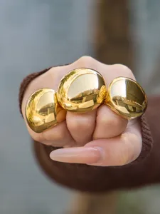 Close-up detail shot of exaggerated gold geometric sphere rings, smooth wide polished finish.