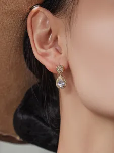 Detalle de pendientes colgantes de circonita en gota, elegante joyería dorada para mujer.