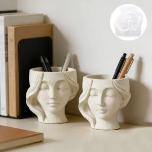 Vue détaille du moule en silicone visage humain et du pot à crayons en plâtre sur le bureau.