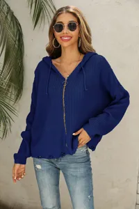 Close-up detail of dark blue knitted zip-up hoodie featuring distressed hem and cozy hood.