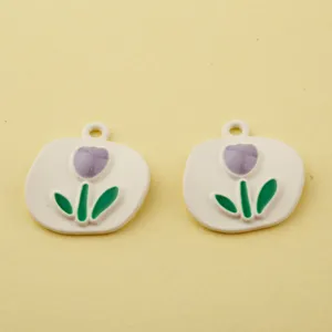 Close up view of white alloy tulip charms with purple enamel and green leaves for DIY jewelry making.