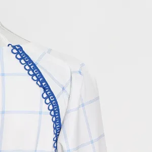 Detalle en primer plano de vestido blanco de manga larga con cuadros azules y ribete de encaje.