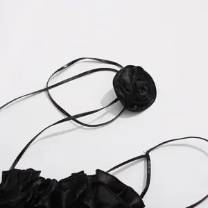 Detalle de vestido halter de satén negro con flor de rosa 3D y elegante tirante de cerca.