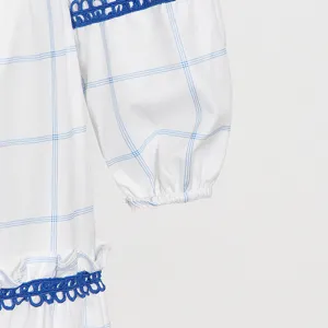 Detalle de vestido a cuadros blanco azul, ribete de encaje dulce y dobladillo con volantes.