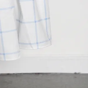Primer plano detalle de tela blanca con patrón de cuadros azules y dobladillo de costura fina.