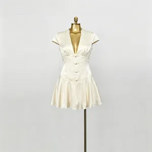 Primo piano del mini abito beige con scollo a V profondo, vita stretta e bottoni delicati.