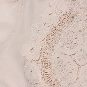 Détail élégant de robe brodée de dentelle beige avec motifs floraux ajourés complexes.