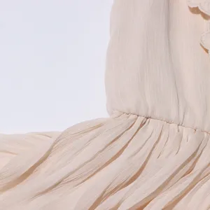 Détail de robe longue plissée beige avec des volants brodés délicats, style élégant.