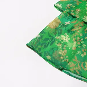 Detalle de vestido de gasa floral verde con hilo metálico y volantes escalonados.