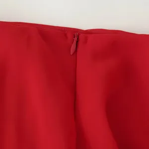 Détail de fermeture éclair de robe en mousseline rouge montrant un travail textile fin.