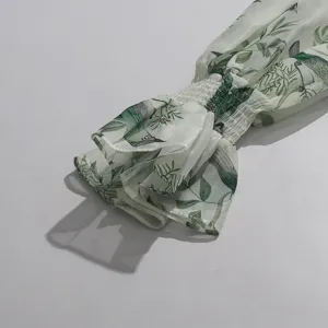 Close-up of women's chiffon long sleeve with green bird floral print and smocked ruffled cuffs.