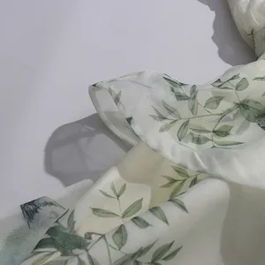 Close-up of green leaf bird print ruffle dress fabric, light cyan floral pattern, soft texture.