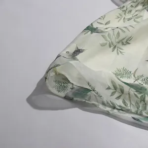 Detailed view of light cyan botanical bird print women dress fabric texture and ruffles layer.