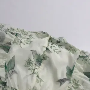 Detail shot of light cyan bird and leaf print dress, showing exquisite fabric texture and ruffles.